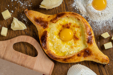 Adjarian Khachapuri with Adyghe cheese and egg yolks and slices of butter is on a wooden board sprinkled with flour.