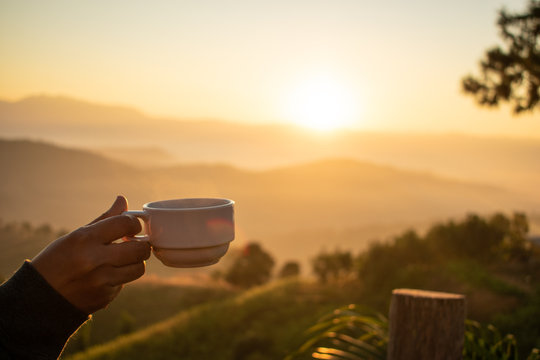 hand holding coffee cup with mountain view and sunrise in the morning,selective focus