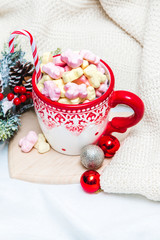 Obraz na płótnie Canvas Red mug with marshmallows and winter ornaments on a white sheets