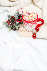 Red mug with marshmallows and winter ornaments on a white sheets