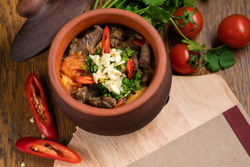 Pot of hungarian goulash on rustic wood background with chili peppers and laurel and copy space