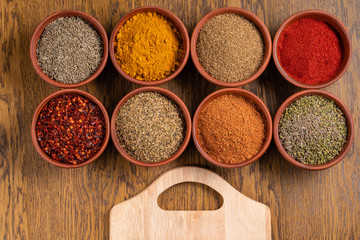 A selection of various colorful spices on a wooden table in bowls