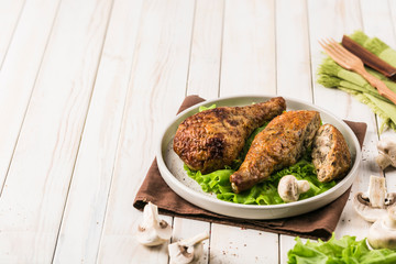 Fried chicken drumstick stuffed with mushrooms flat plate with lettuce leaf on light wooden background.
