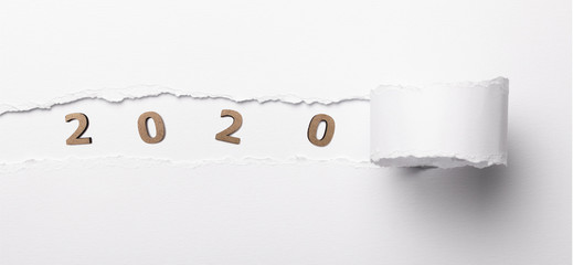 colored background with wooden figure of the date 2020 in a hole of torn cardboard, concept new year from scratch, calendar cover