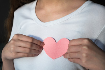 Woman in white t-shirt holding pink paper heart against chest