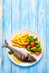 Roast fish with french fries and vegetable on wooden background