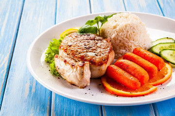 Roast steak with white rice and vegetables on wooden background