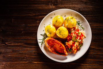 Fried chicken breast with boiled potatoes and vegetables on timber background