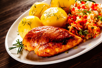 Fried chicken breast with boiled potatoes and vegetables on timber background