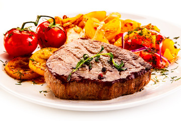 Grilled steak with fried potatoes and vegetables on white background