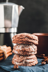 Chocolate cookies, cup with coffee, moka pot, cinnamon sticks, star anise on blue napkin, dark background with copy space