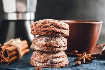 Chocolate cookies, cup with coffee, moka pot, cinnamon sticks, star anise on blue napkin, dark background with copy space