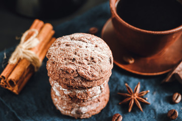 Homemade bakery, chocolate cookies with powdered sugar, brown cup with coffee, cinnamon sticks, star anise on blue napkin