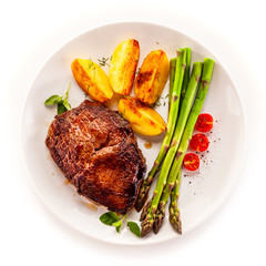 Barbecued beef steak with asparagus and fried potatoes on white background