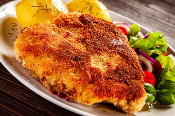 Schnitzel with boiled potatoes on timber background