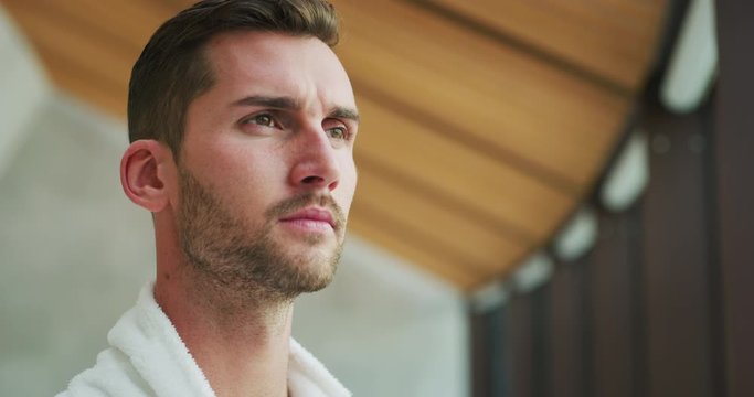 Portrait of an young man in white bathrobe is drinking a hot tea after various treatments in a relax room of a luxury wellness center.
