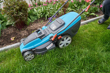 Obraz na płótnie Canvas An electric lawn mower cuts the lawn near the edge and concrete curb. Close-up