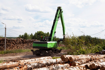 Obraz premium A reloader (excavator) in the open warehouse of logs for a plywood factory