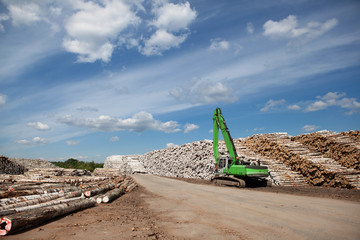 A reloader (excavator) in the open warehouse of logs for a plywood factory