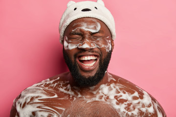 Spa, hygiene and relax concept. Naked black unshaven man takes shower with foam, has fun in...
