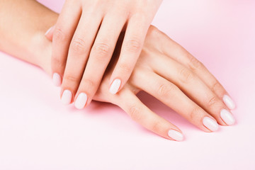 Obraz na płótnie Canvas Female's hands with classic pastel manicure on pink background. Beauty salon.