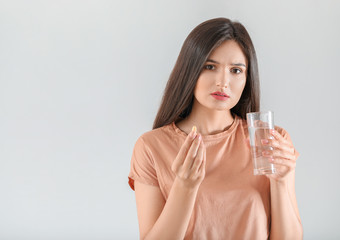 Young woman taking pill on light background