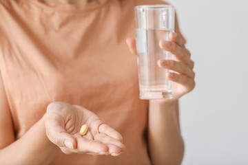 Young woman taking pill on light background, closeup