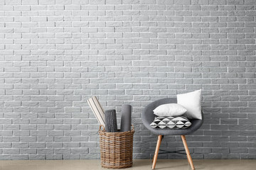Soft armchair with pillows and basket near brick wall