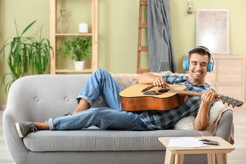 Obraz premium Handsome man with guitar listening to music at home