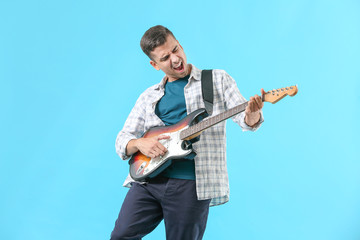 Handsome emotional man playing guitar on color background