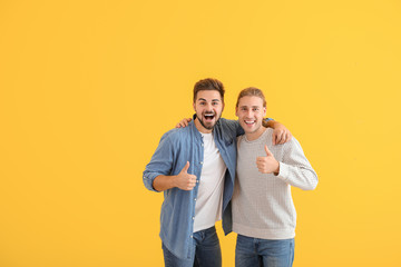 Fototapeta premium Happy friends showing thumb-up gesture on color background