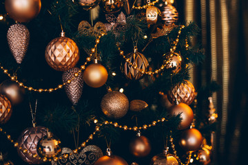 Fir branch with golden balls and festive lights on the dark background with sparkles.