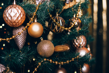 Fir branch with golden balls and festive lights on the dark background with sparkles.
