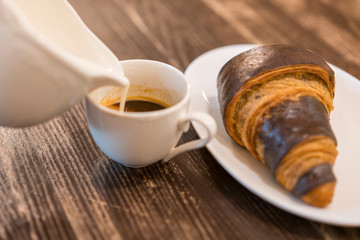 Cream is poured into coffee. Croissant on a table in a cafe. Breakfast concept