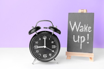 Alarm clock and chalkboard with text WAKE UP on table