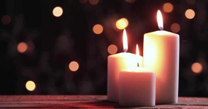 Three white Christmas candles on the wooden table with blurred sparkling light background. Shot in 4k resolution