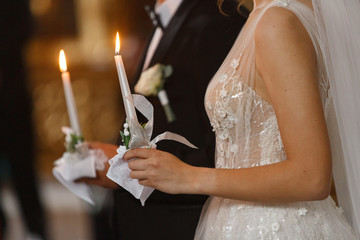 bride and groom holding candles with light during wedding ceremony in christian church.