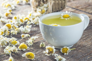 white cup of chamomile tea with dry daisy flowers on rustic wooden background, herbal medicine hot drink concept