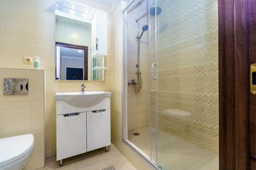 Bathroom in the apartment. Shower, sink with mirror, toilet. Square ceramic tiles in the form of white and yellow scalloped patterns on the wall in the bathroom. 