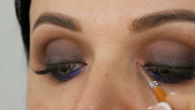 Makeup artist makes models smoky eyes with the help of special brush Lilac and pearly smoky eyes eyeshadow, eyes and face of a woman close up view. Professional high fashion.
