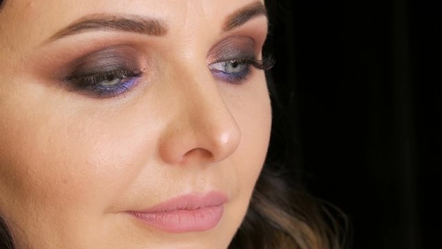 Pensive face of a beautiful young woman with professional makeup in lilac tones, smoky eyes, close-up view
