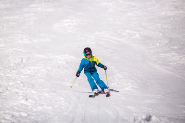 Fototapeta na wymiar Little girl in blue and yellow ski costume skiing in downhill slope. Winter sport recreational activity