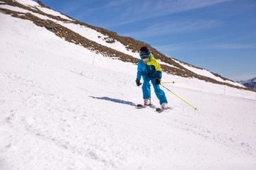 Fototapeta na wymiar Little girl in blue and yellow ski costume skiing in downhill slope. Winter sport recreational activity