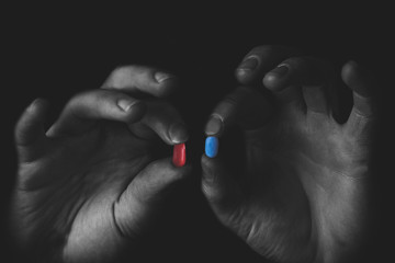 Man holding red and blue pills in hand isolated on black background.  Medicine concept and pills,...