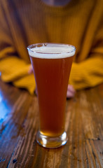 glass of beer with a woman and her hands folded in the background
