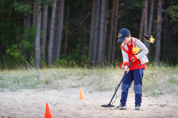 Photograph of boy using a metal detector to search for lost treasure on a beach - 306608307