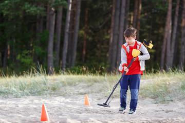 Photograph of boy using a metal detector to search for lost treasure on a beach