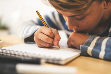 Student drawing with pencil on the notebook. Boy doing homework writing on a paper. Kid hold a...