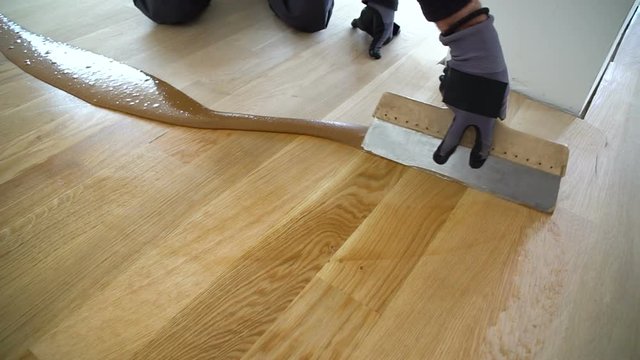 Carpenter master with gloves grouting wooden parquet, phase after sanding. Varnishing of oak parquet floor, man workers with hand and spatula