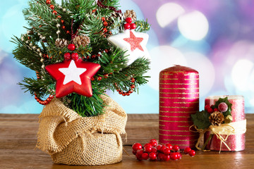 small christmas tree decorated with stars next to beautiful candles and red berries on wooden table with christmas lights in the background